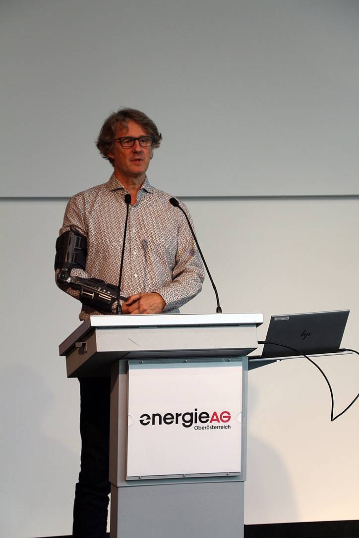 Mann mit Armschiene spricht am Rednerpult mit Energie AG Oberösterreich Logo